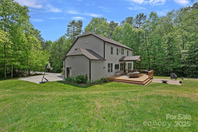 rear view of property with an outdoor fire pit, a wooden deck, a lawn, and roof with shingles