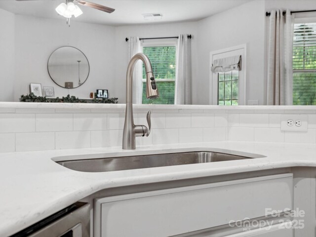 kitchen view of a sink, a ceiling fan, and white cabinetry