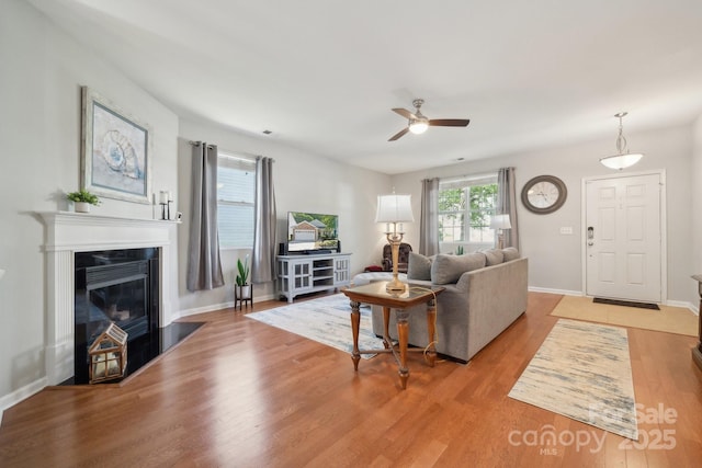 living room featuring a ceiling fan, light wood-style flooring, a glass covered fireplace, and baseboards