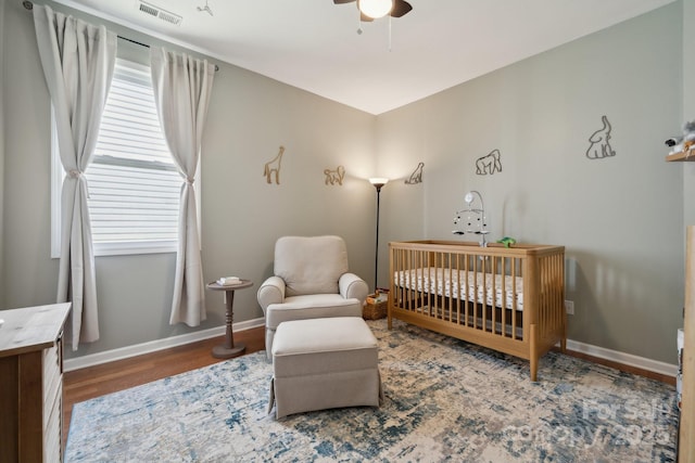 bedroom featuring a crib, wood finished floors, baseboards, and a ceiling fan