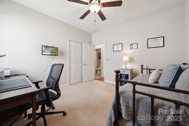 bedroom with a desk, light colored carpet, baseboards, a closet, and a ceiling fan