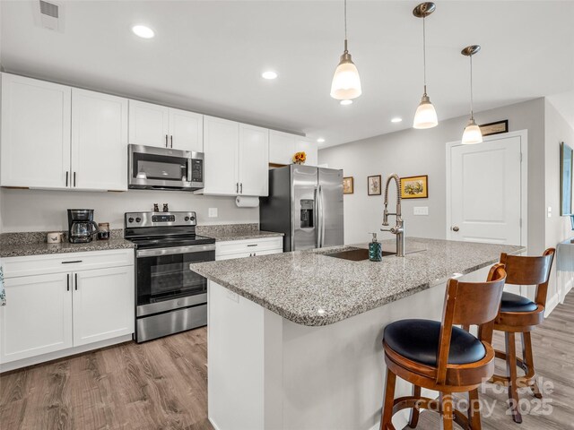 kitchen with stainless steel appliances, a sink, light wood-type flooring, a kitchen breakfast bar, and recessed lighting