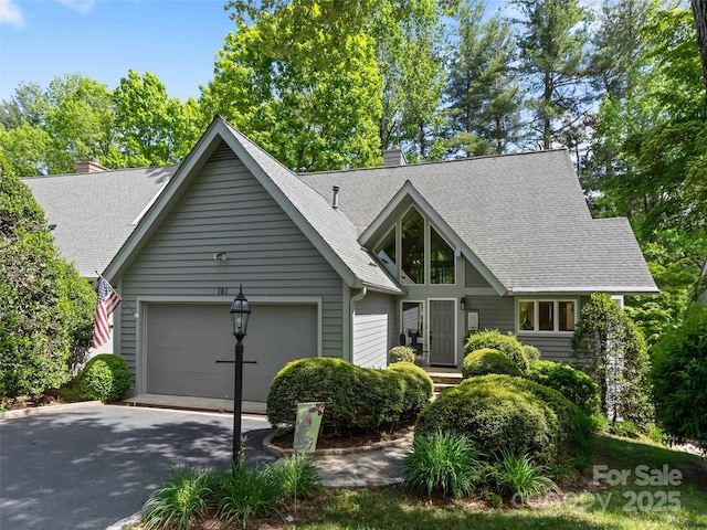 view of front of property featuring driveway, a shingled roof, a garage, and a chimney