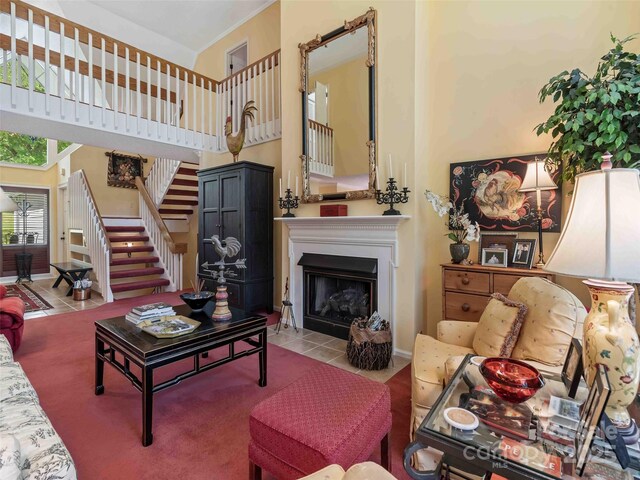 living room featuring stairs, a towering ceiling, tile patterned flooring, and a fireplace with flush hearth