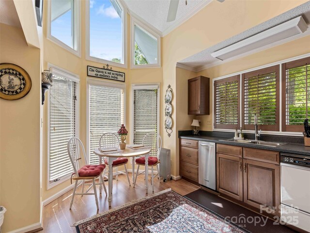 kitchen with a sink, dishwasher, ornamental molding, dark countertops, and light wood-style flooring