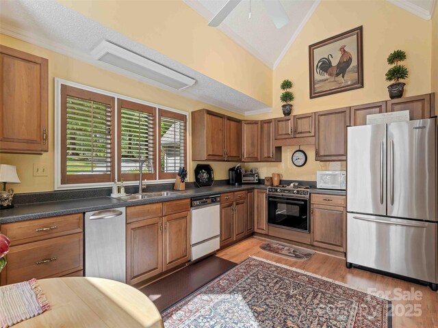 kitchen with white appliances, a sink, light wood-style floors, dark countertops, and brown cabinetry