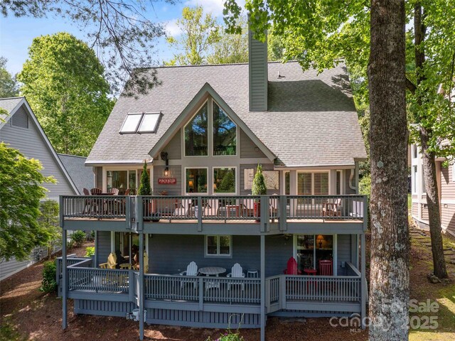 back of property with a chimney, roof with shingles, and a deck