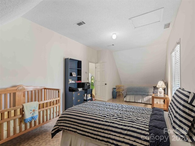 bedroom with lofted ceiling, attic access, and a textured ceiling
