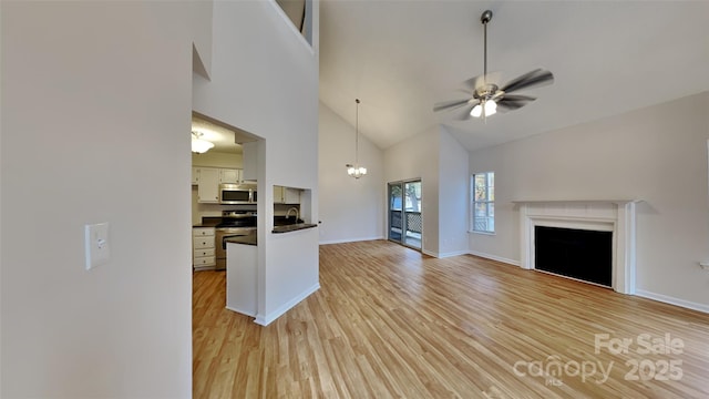 unfurnished living room with high vaulted ceiling, light wood-style floors, a sink, a ceiling fan, and a fireplace