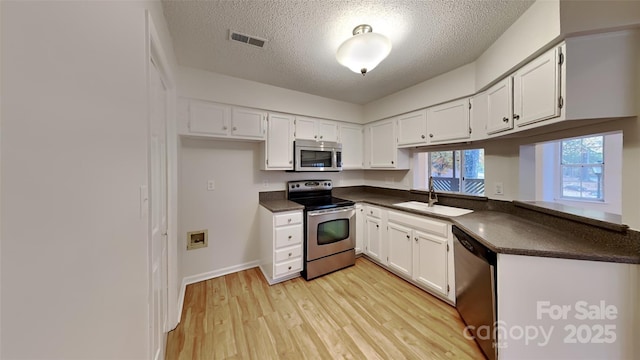 kitchen with stainless steel appliances, a sink, dark countertops, a textured ceiling, and white cabinetry