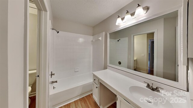 bathroom featuring wood finished floors, vanity, toilet, a textured ceiling, and shower / washtub combination