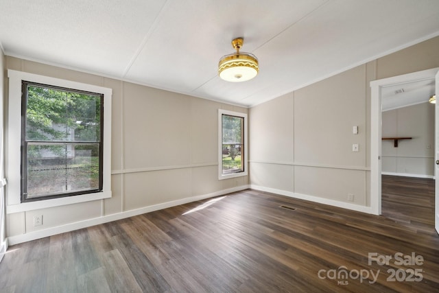 spare room featuring wood finished floors, plenty of natural light, a decorative wall, and lofted ceiling