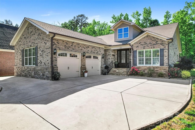 view of front of home featuring an attached garage, driveway, roof with shingles, brick siding, and stone siding