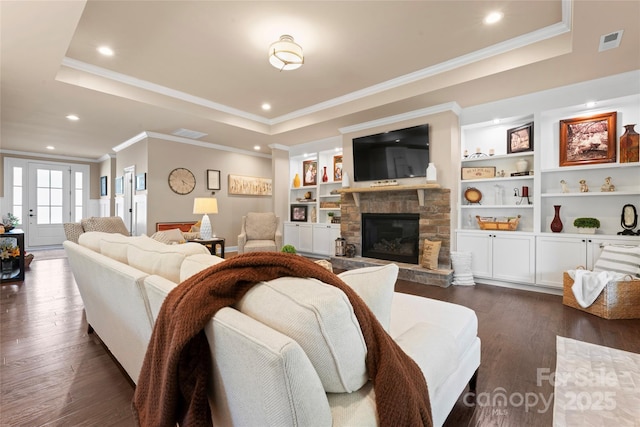 living area with a tray ceiling, dark wood finished floors, a stone fireplace, ornamental molding, and baseboards