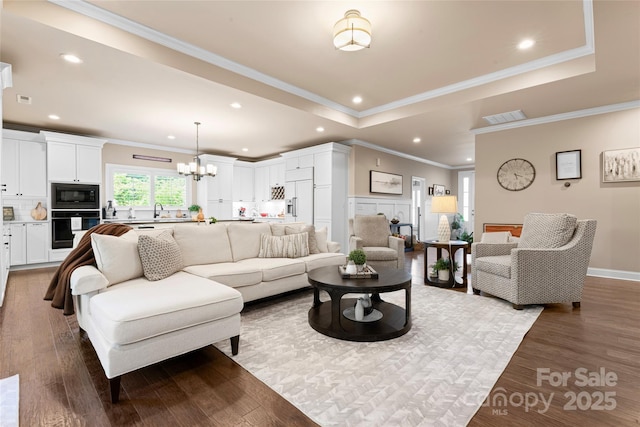 living area featuring a raised ceiling, recessed lighting, a chandelier, wood finished floors, and ornamental molding