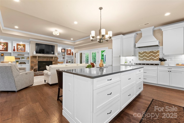 kitchen with custom range hood, a raised ceiling, a chandelier, stovetop, and a fireplace