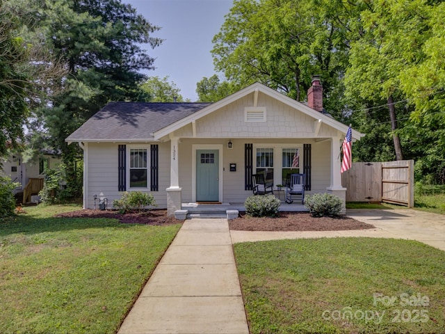 bungalow-style house featuring a chimney, covered porch, and roof with shingles