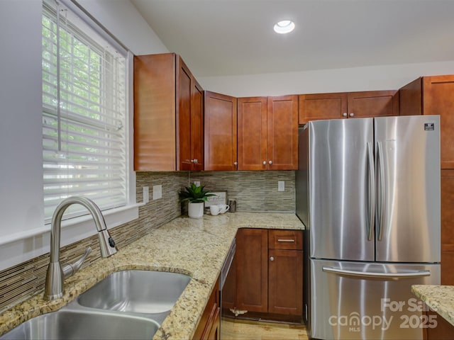 kitchen featuring stainless steel appliances, a sink, tasteful backsplash, light stone countertops, and light wood finished floors