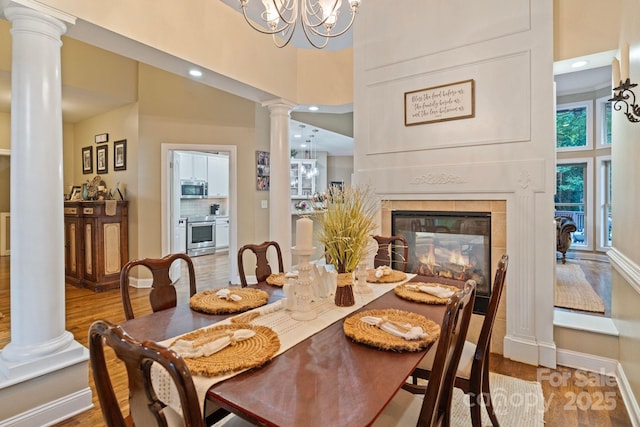 131 Sierra Woods Dr, Troutman, NC 28166 - dining space featuring ornate columns, a towering ceiling, wood finished floors, a chandelier, and a tiled fireplace
