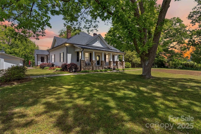 back of property at dusk with covered porch, a chimney, a yard, and a garage