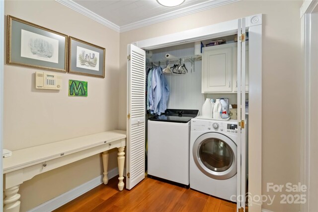 laundry area featuring washing machine and clothes dryer, cabinet space, wood finished floors, ornamental molding, and baseboards