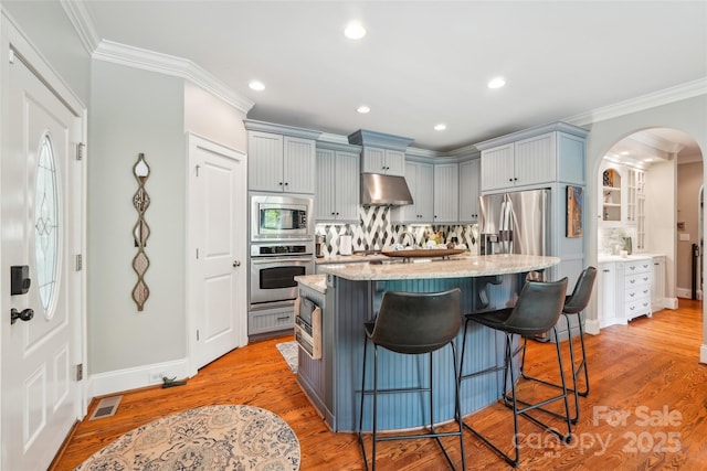 1701 Dearmon Dr, Charlotte, NC 28205 - kitchen featuring appliances with stainless steel finishes, under cabinet range hood, light stone counters, arched walkways, and decorative backsplash