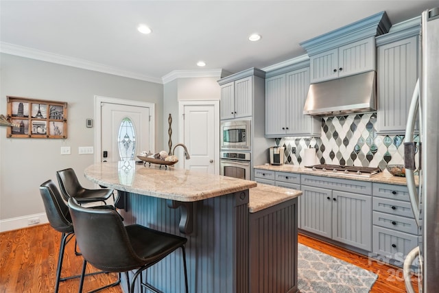 1701 Dearmon Dr, Charlotte, NC 28205 - kitchen with appliances with stainless steel finishes, under cabinet range hood, gray cabinetry, ornamental molding, and a center island with sink