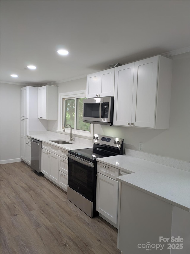 kitchen with stainless steel appliances, a sink, wood finished floors, white cabinets, and recessed lighting