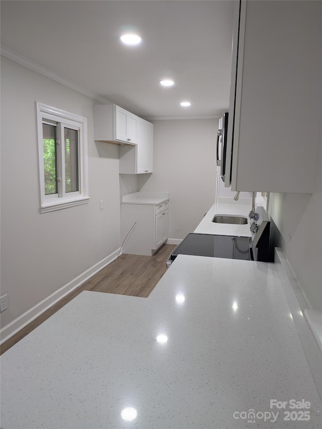 kitchen with ornamental molding, white cabinets, light wood-type flooring, light stone countertops, and baseboards