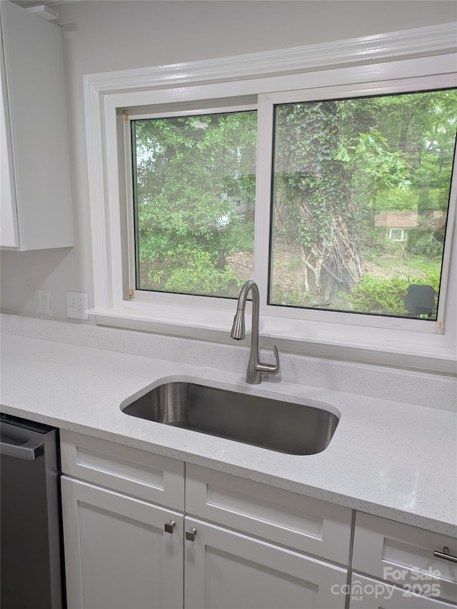 kitchen with a sink, white cabinetry, stainless steel dishwasher, and light stone countertops