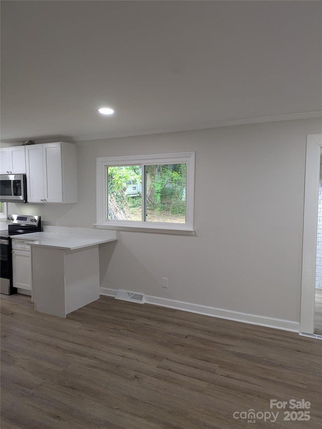 kitchen featuring appliances with stainless steel finishes, a peninsula, white cabinets, dark wood-type flooring, and baseboards
