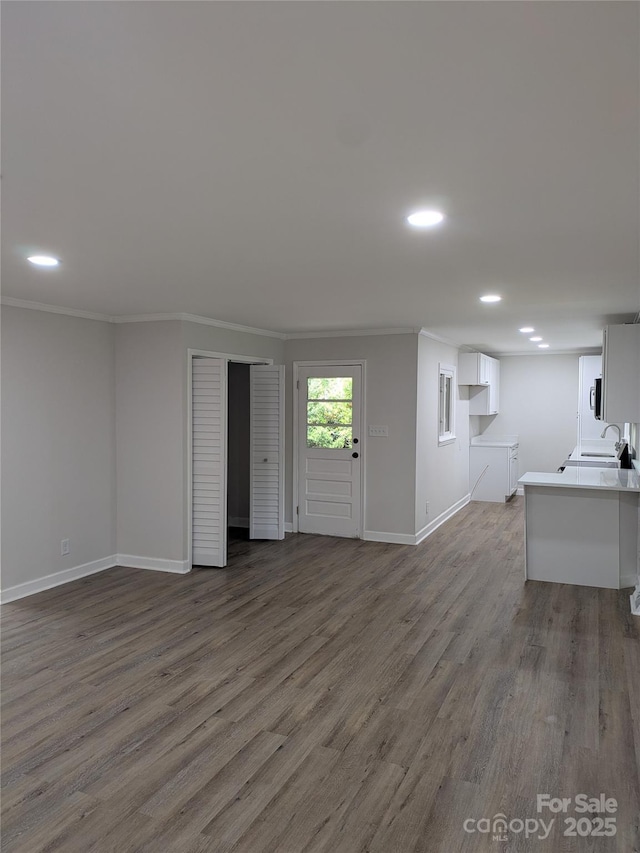 unfurnished living room featuring a sink, crown molding, wood finished floors, baseboards, and recessed lighting