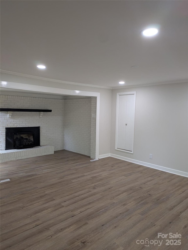 below grade area with dark wood-type flooring, a fireplace, baseboards, recessed lighting, and ornamental molding