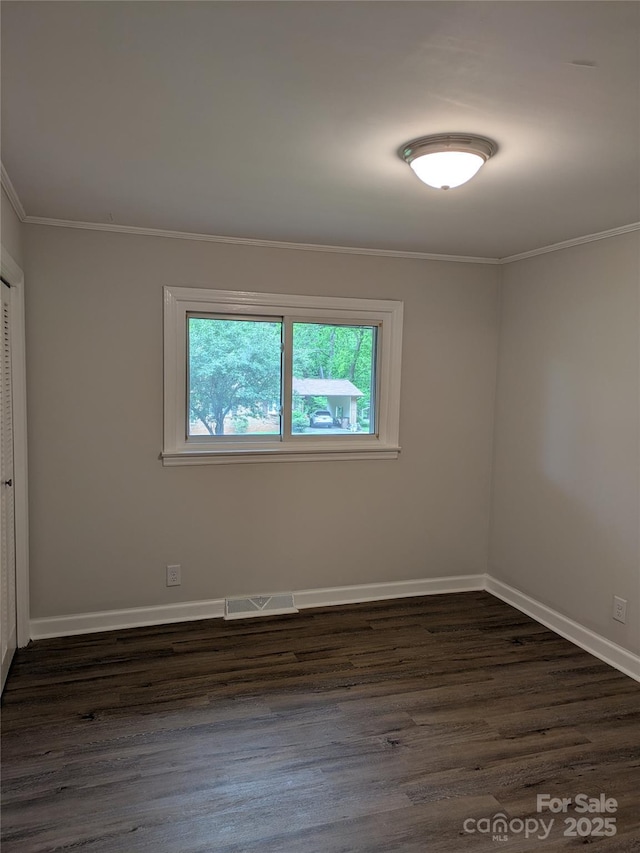 empty room featuring ornamental molding, dark wood-style floors, and baseboards