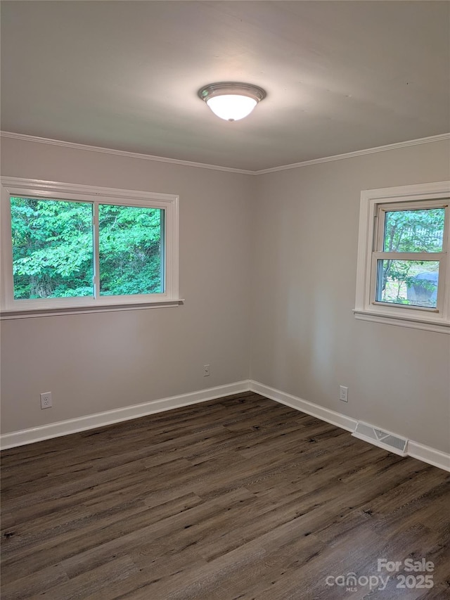 empty room featuring healthy amount of natural light, dark wood-style flooring, crown molding, and baseboards