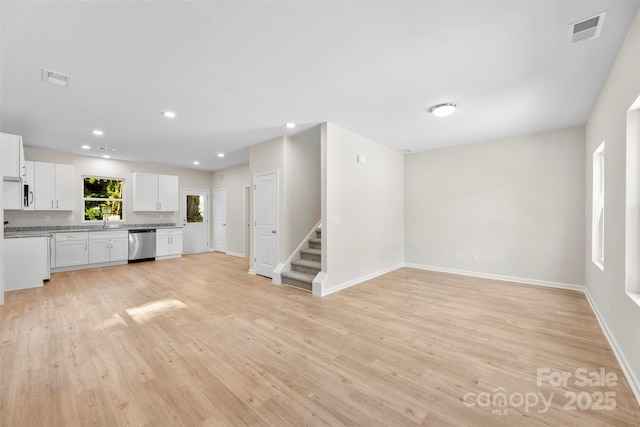 unfurnished living room featuring light wood finished floors, stairway, baseboards, recessed lighting, and a sink