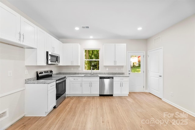 kitchen with appliances with stainless steel finishes, a sink, white cabinetry, light wood-style flooring, and recessed lighting