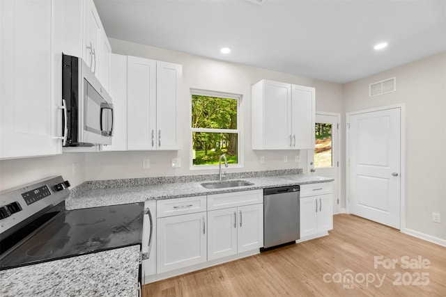 kitchen with appliances with stainless steel finishes, a sink, light wood-type flooring, white cabinetry, and light stone counters