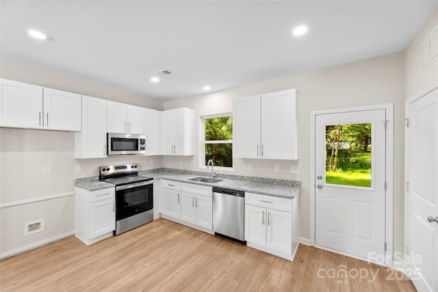 kitchen with appliances with stainless steel finishes, a sink, light wood-style floors, white cabinets, and recessed lighting