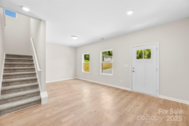 unfurnished living room with healthy amount of natural light, stairway, light wood-style flooring, baseboards, and recessed lighting