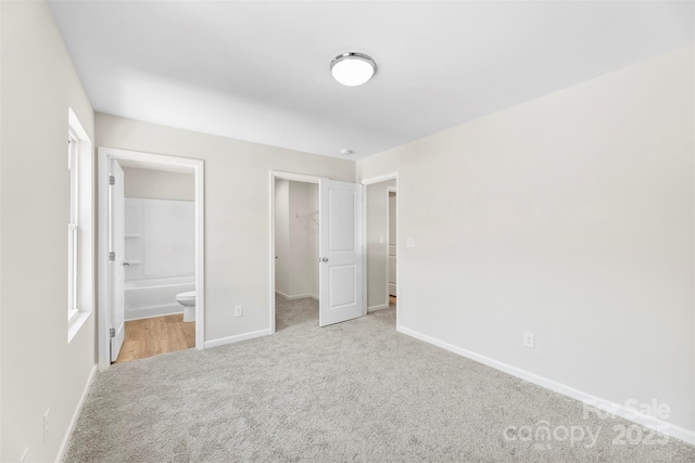 unfurnished bedroom featuring carpet flooring, baseboards, a walk in closet, ensuite bath, and a closet