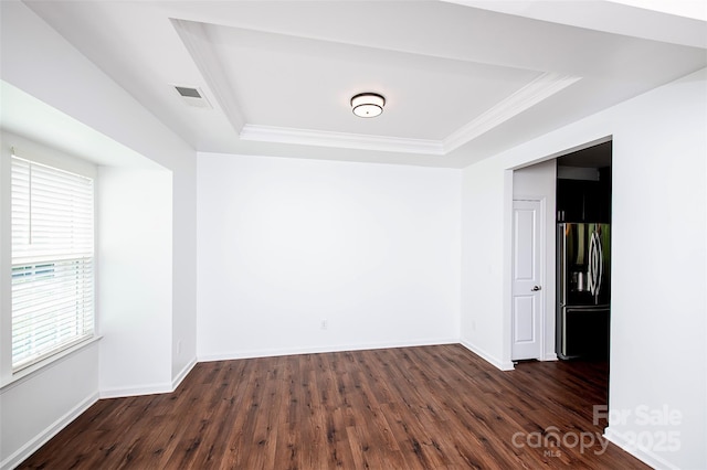 spare room featuring a raised ceiling, dark wood-type flooring, crown molding, and baseboards