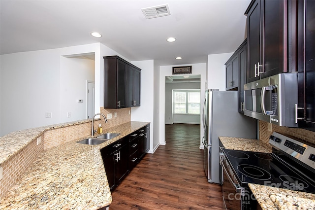 kitchen with appliances with stainless steel finishes, a sink, dark wood-style floors, backsplash, and light stone counters