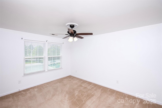 spare room with light carpet, a ceiling fan, and baseboards