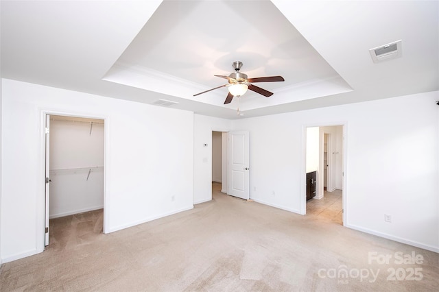 unfurnished bedroom featuring a raised ceiling, baseboards, light colored carpet, a walk in closet, and crown molding