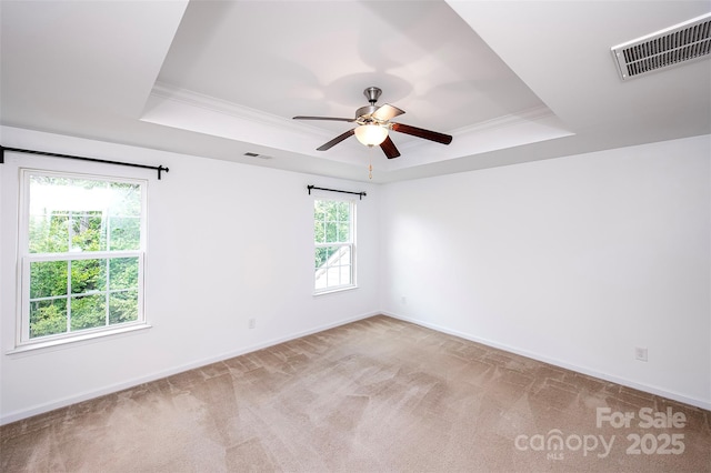 unfurnished room with a raised ceiling, ceiling fan, light colored carpet, baseboards, and ornamental molding