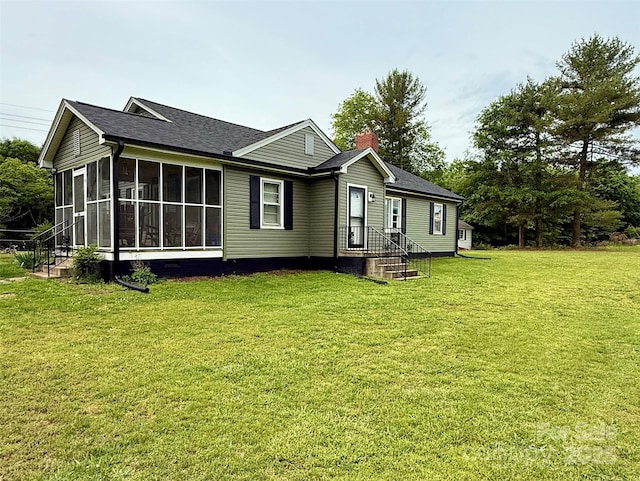 back of house featuring a sunroom, a lawn, a chimney, and roof with shingles
