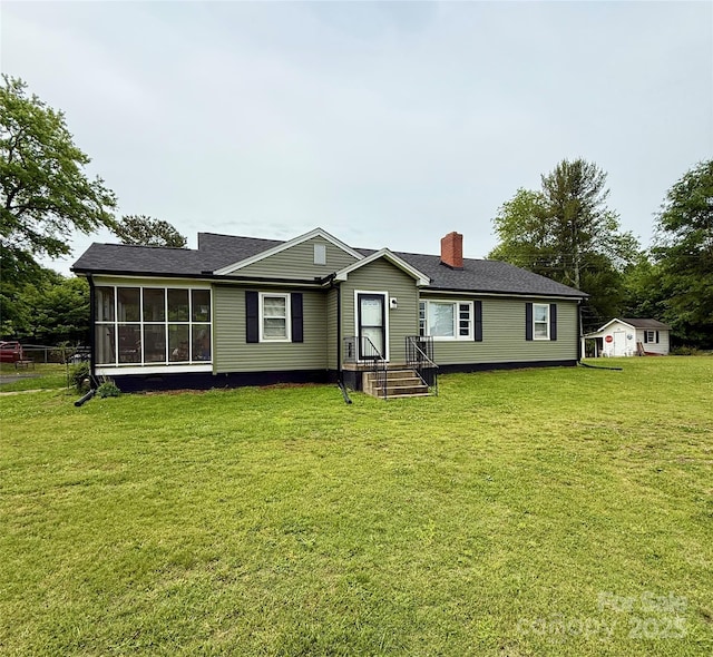 rear view of house with a chimney, a lawn, a sunroom, and roof with shingles