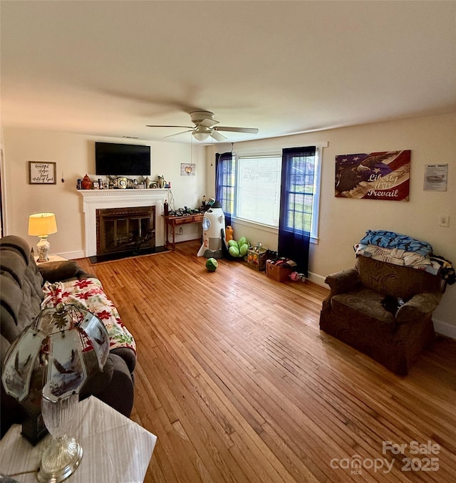 living area with hardwood / wood-style floors, ceiling fan, and a glass covered fireplace