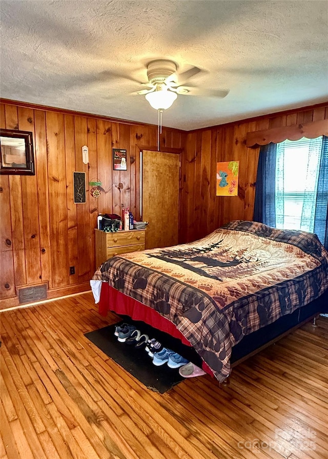 bedroom with a textured ceiling, hardwood / wood-style floors, and wooden walls